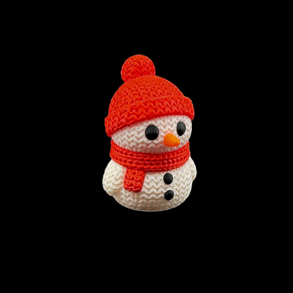 Cute snowman figurine wearing a red knit hat with pom-pom and matching scarf, featuring black button eyes, a small orange carrot nose, and black button details.